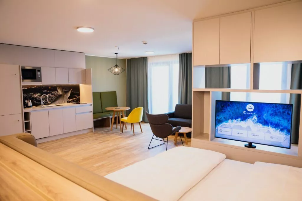 Doppelbett mit weißem Laken neben Küchenzeile und Sessel