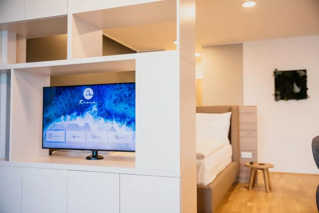 TV vor großem Bett mit weißem Laken