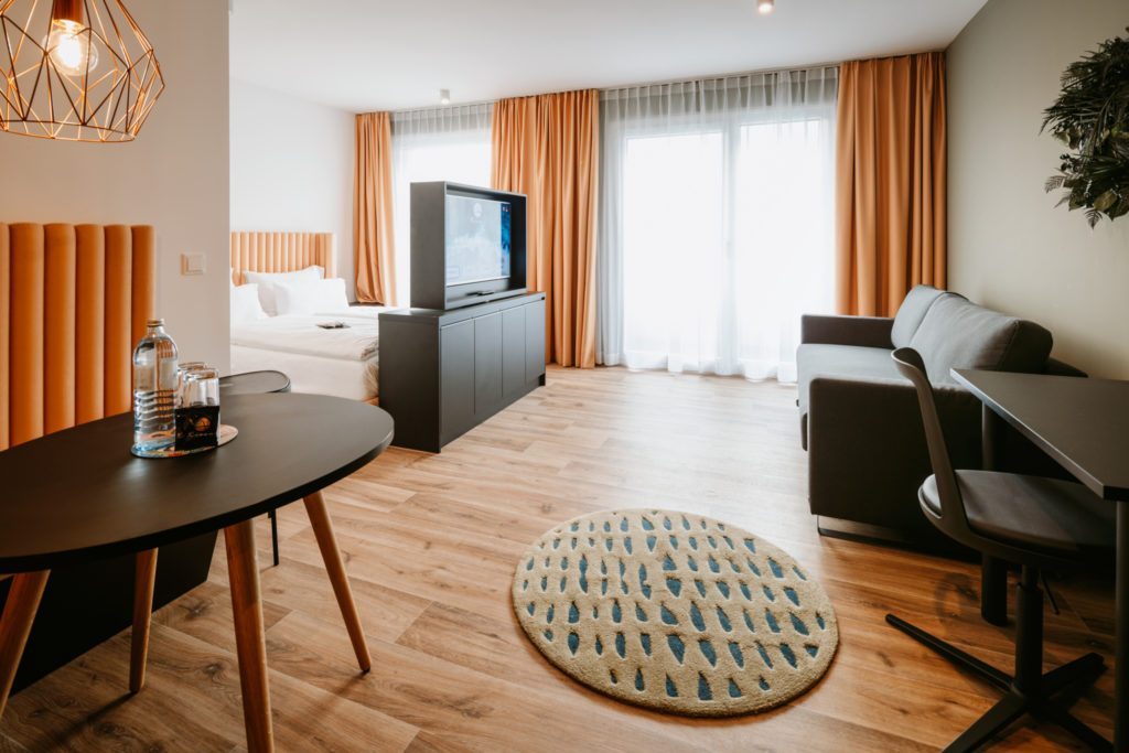 TV vor Doppelbett und Couch grau