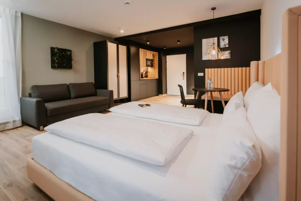 Doppelbett mit weißem Laken vor Sofa und Schrank