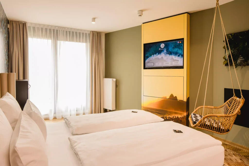 Doppelbett mit weißem Laken vor großem Fenster in modernem Hotelzimmer