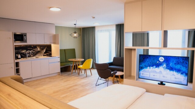 Doppelbett mit weißem Laken neben Küchenzeile und Sessel