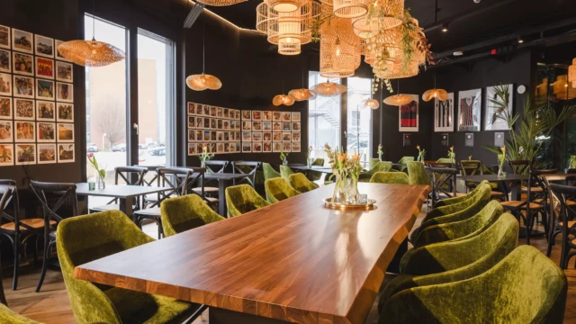 Großer Holztisch mit grünen Stühlen in einer Hotellobby, im Hintergrund weitere Sitzgelegenheiten und dekorative Elemente.