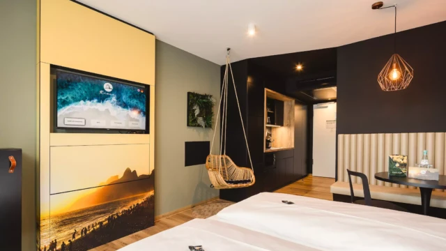 Hotelzimmer in Design Hotel mit großem Doppelbett. Im Hintergrund befindet sich eine moderne Küchenzeile in Schwarz und Holzakzenten.