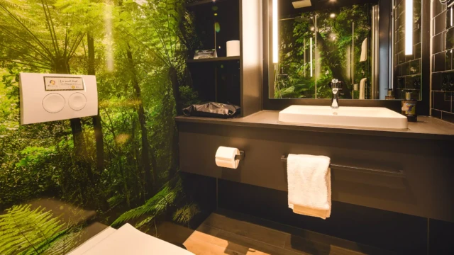 Hotelbad mit Toilette und Waschbecken. Die Rückwand hat ein grünes Dschungel-Design.