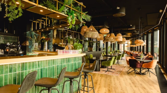 Bar mit grünen Fließen und schwarzen Barhockern