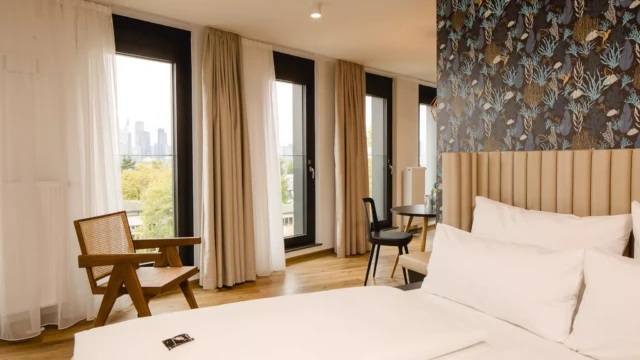 Doppelbett vor großer Fensterfront mit Aussicht über Skyline Frankfurt