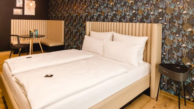 Doppelbett mit weißem Laken vor bunter Tapete